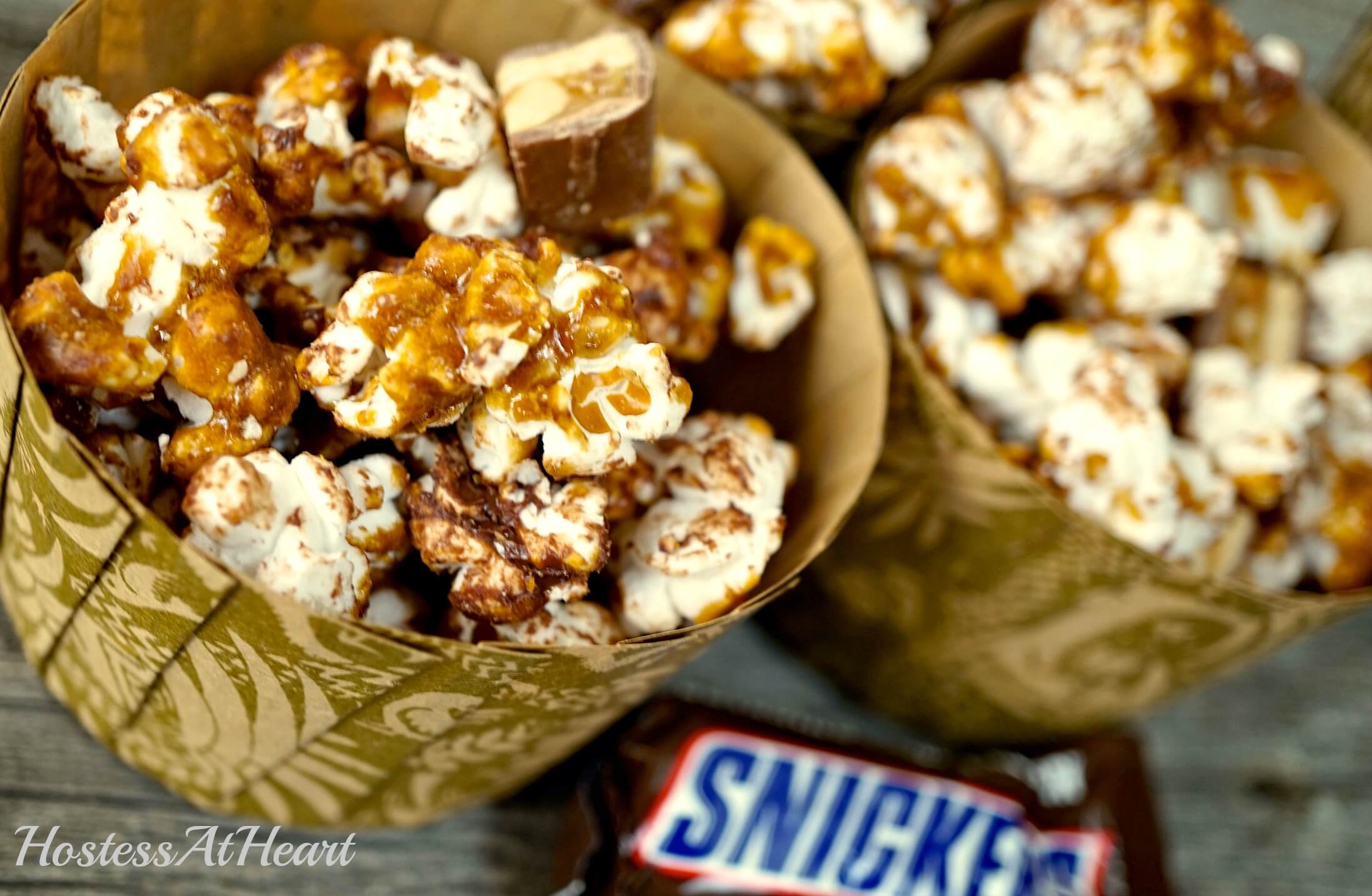 Candy bar Popcorn sitting in cups over a wooden background. A Snickers candy bar sits off to the side.