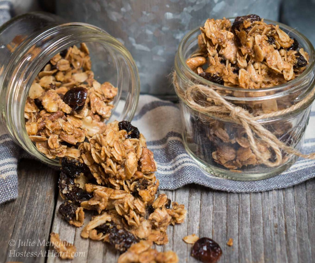 Two serving jars sitting in the front of a large tin of granola with. One jar tipped over and spilling out.