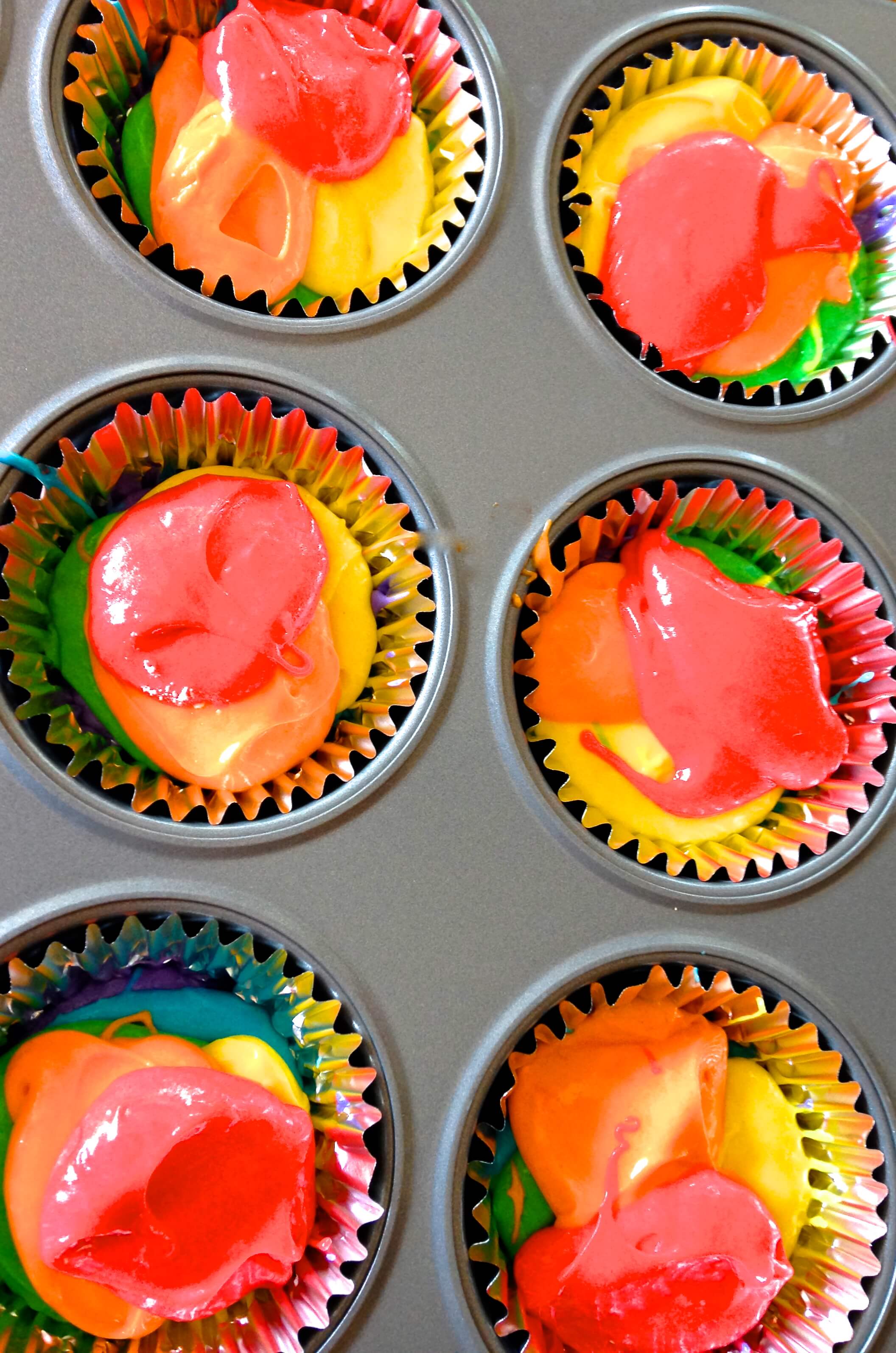 Multi-colored batter filled cupcake papers ready for baking.