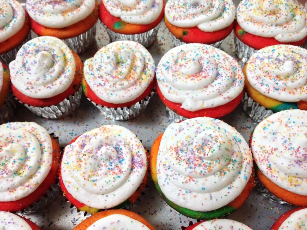 Top view of rainbow dyed cupcakes with swirled frosting and rainbow sprinkles.