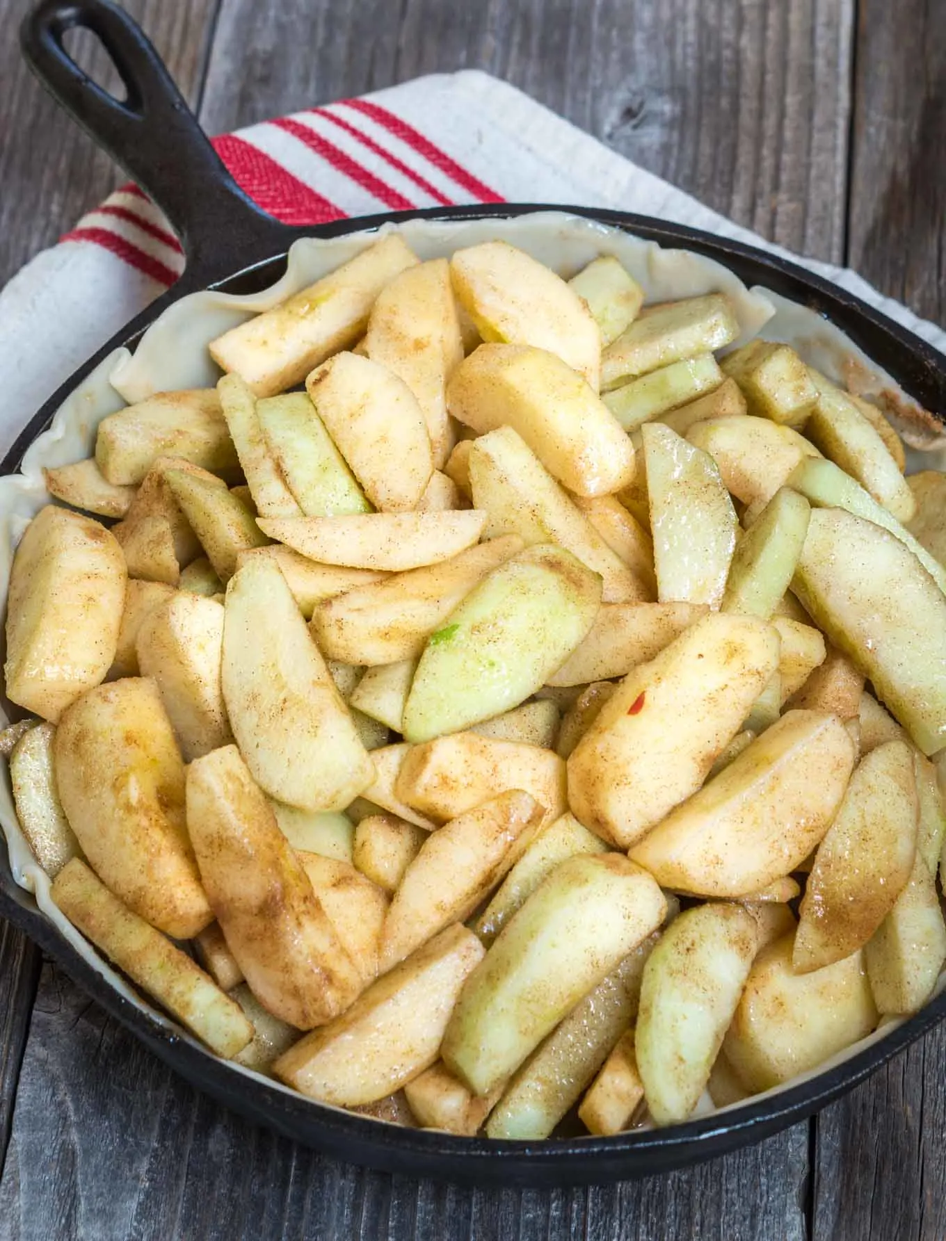 Sliced apples sitting on top of a pie crust in a cast iron skillet 