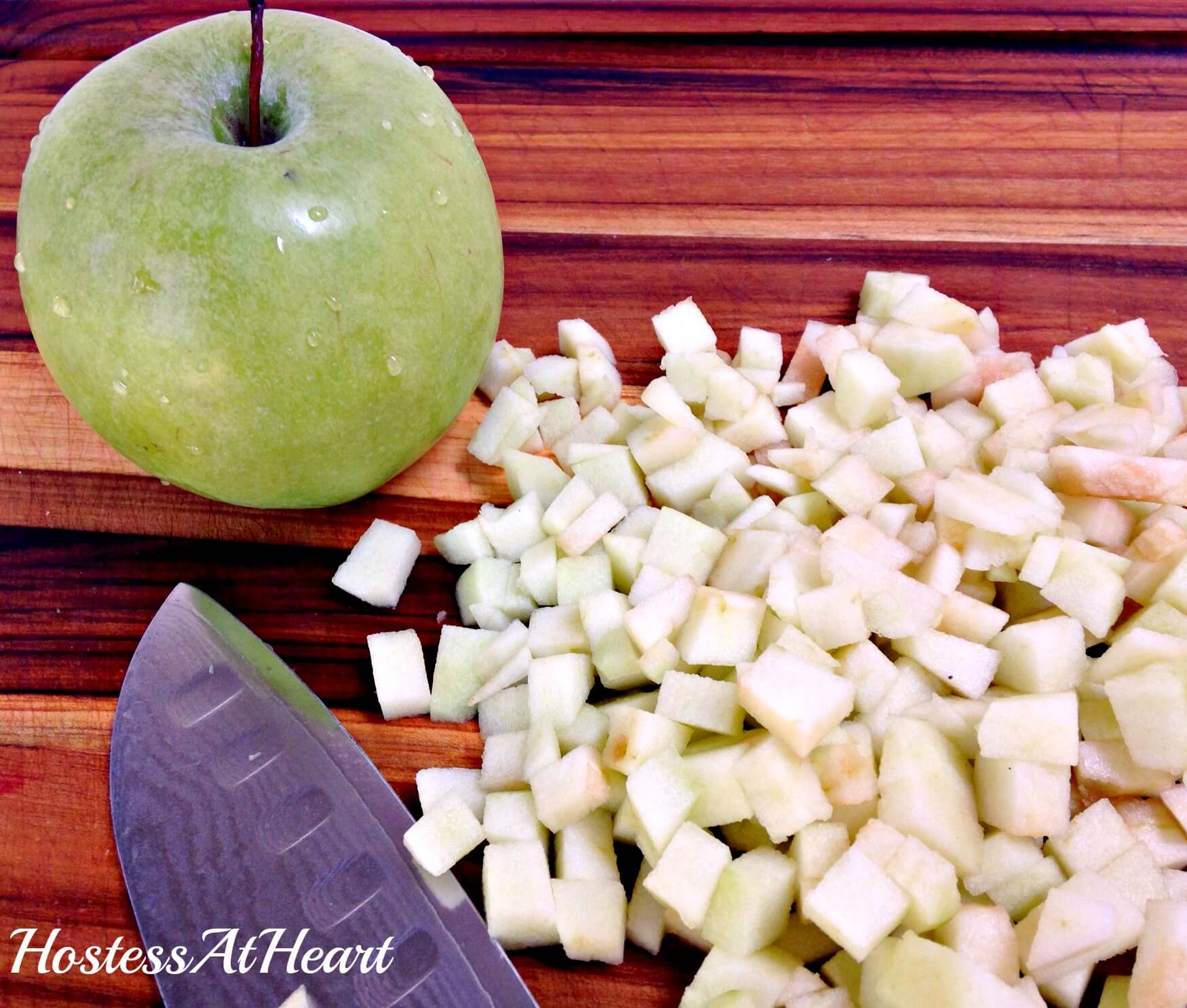 A diced green apples and a knife sit next to a green apple.
