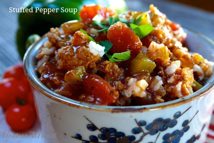 Sideview of a soup bowl with a blue design on the front is heaped with Stuffed Pepper Sour that\'s full of sausage, peppers, tomatoes, and garnished with fresh parsley. Fresh peppers and tomatoes sit in the background. The title \"Stuffed Pepper Soup\" appears in the upper left corner. 