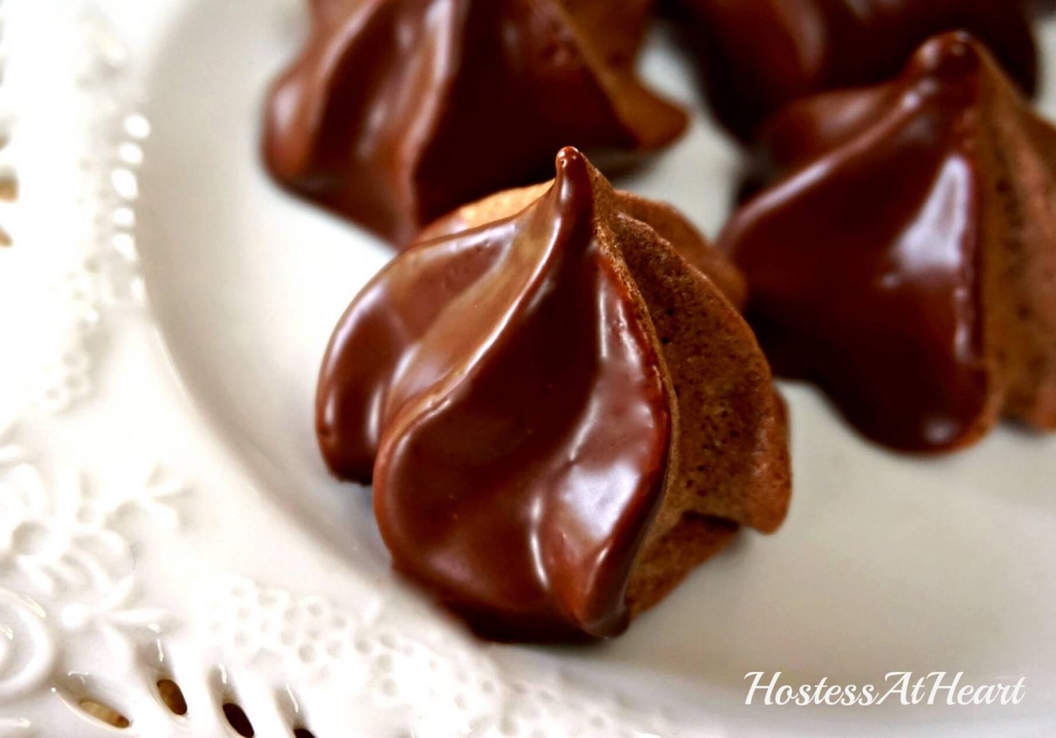 Chocolate Meringue Stars dipped in chocolate ganache sitting on a white plate.