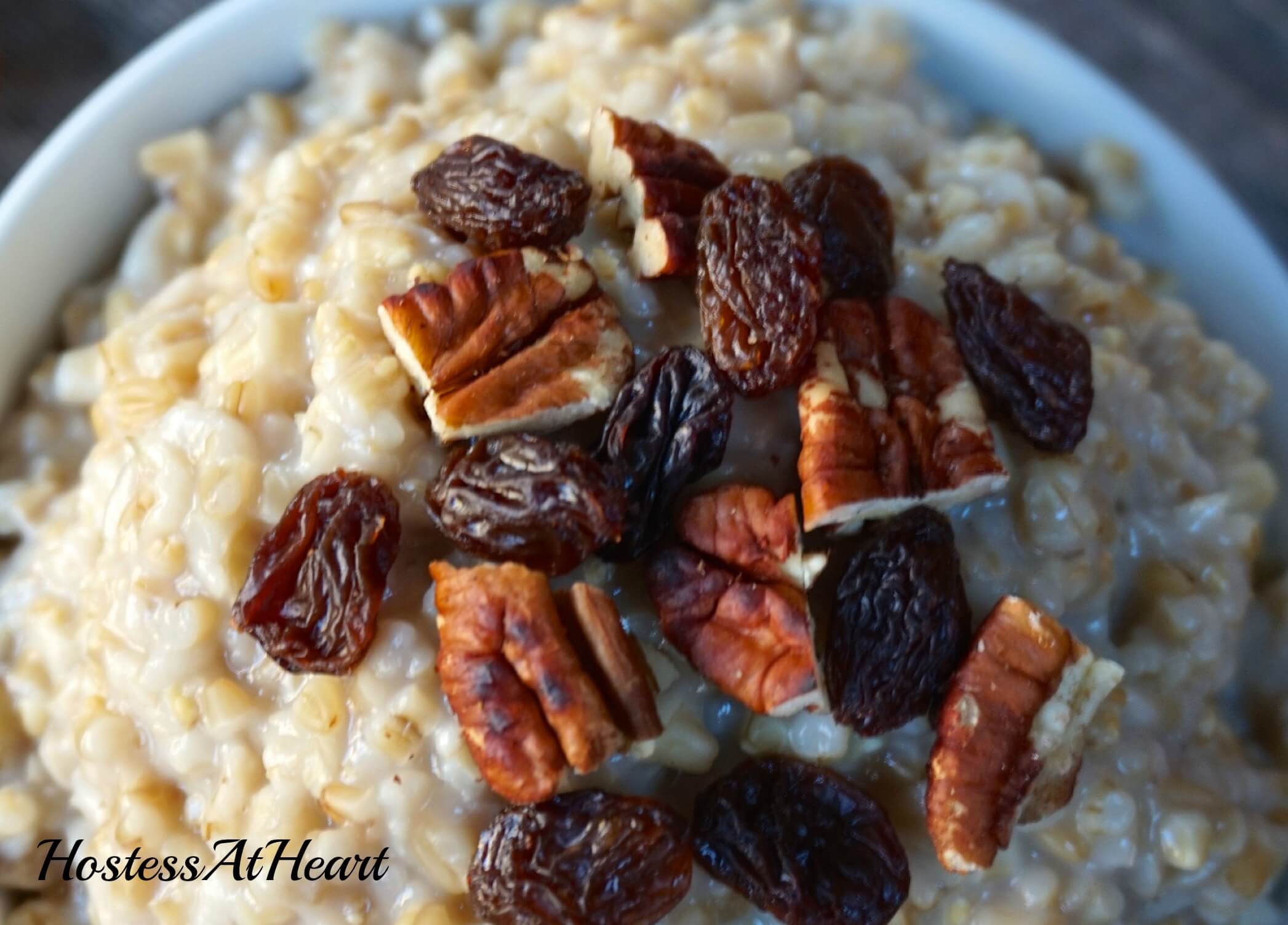 A white bowl filled with Steel Cut Oatmeal and garnished with raisins and chopped pecans.  