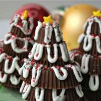 Three Christmas trees made from Reeses Peanut Butter cups with Ornaments in the background.