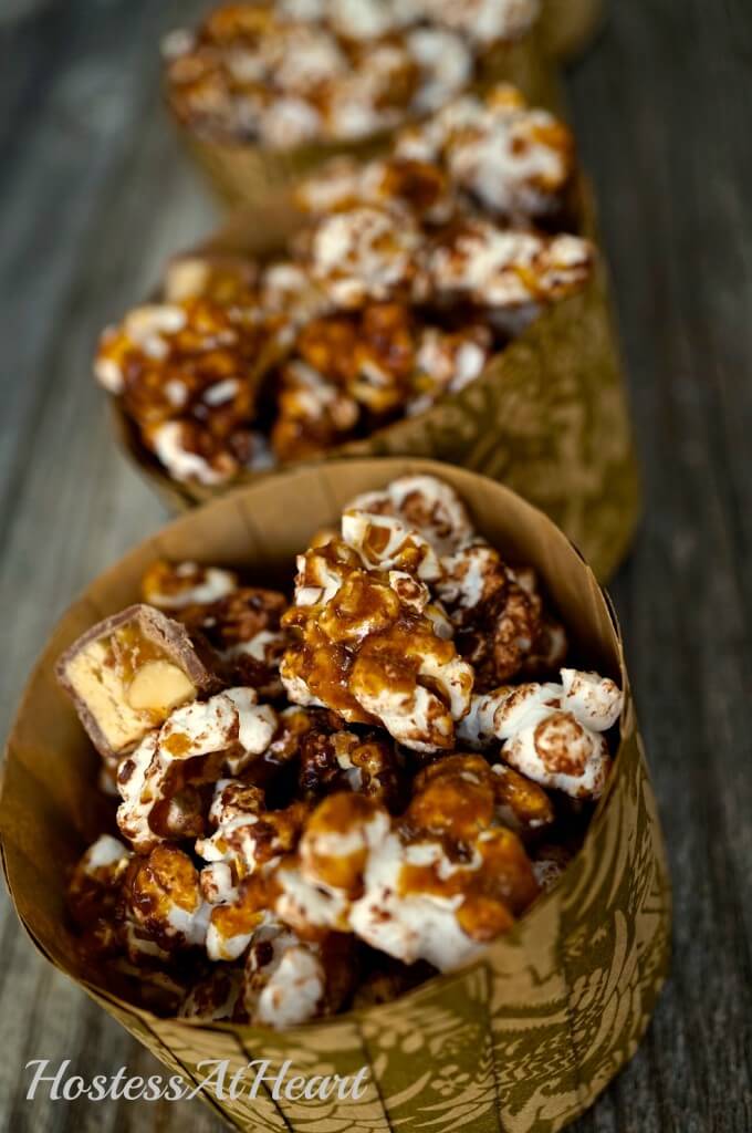 Candy bar Popcorn sitting in cups over a wooden background.