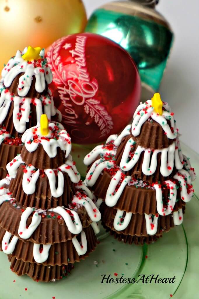 Top view of three Christmas trees made from Reeses Peanut Butter cups with Ornaments in the background.