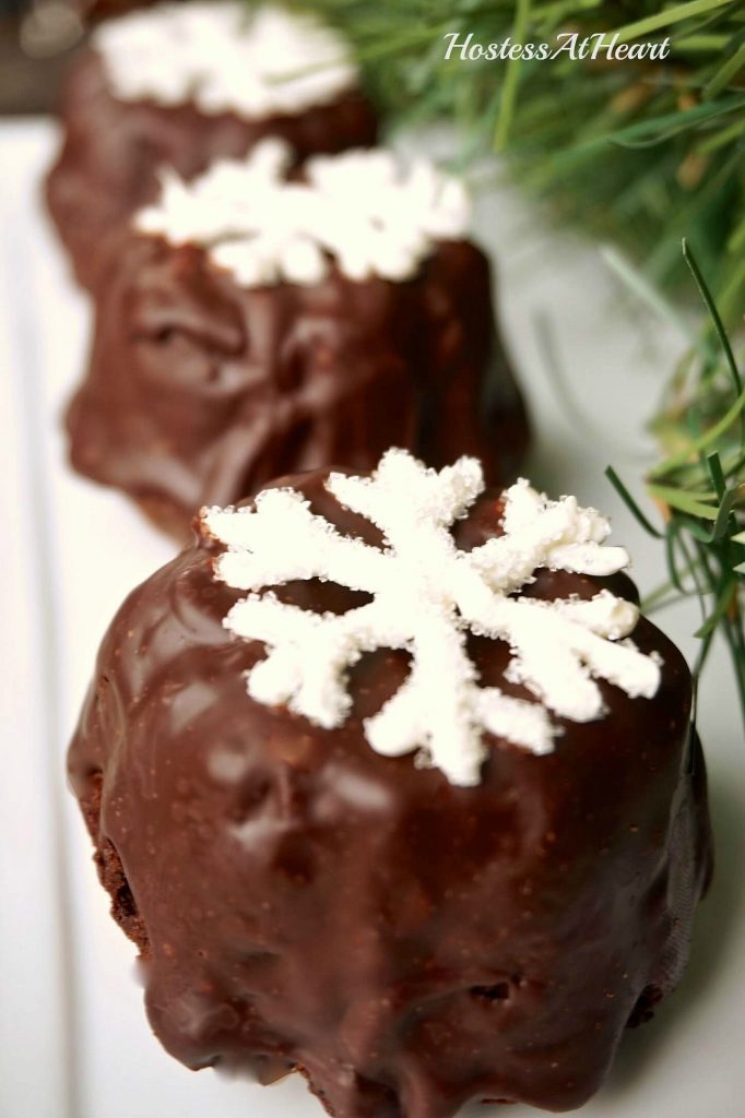 Small cake bundtlettes frosted with chocolate ganache and topped with a sugar snowflake.