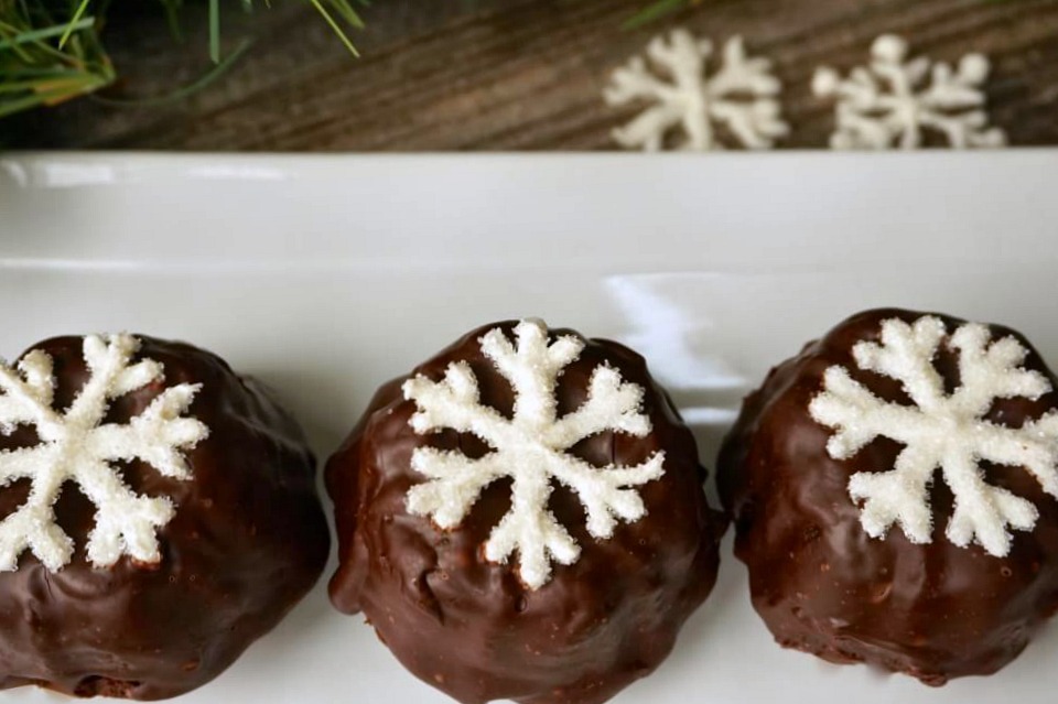 A white plate holding small cake bundtlettes frosted with chocolate ganache and topped with a sugar snowflake.