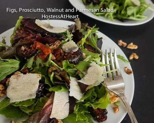 A white plate filled with mixed greens, shaved parmesan, and walnuts. a fork sits next to the plate.