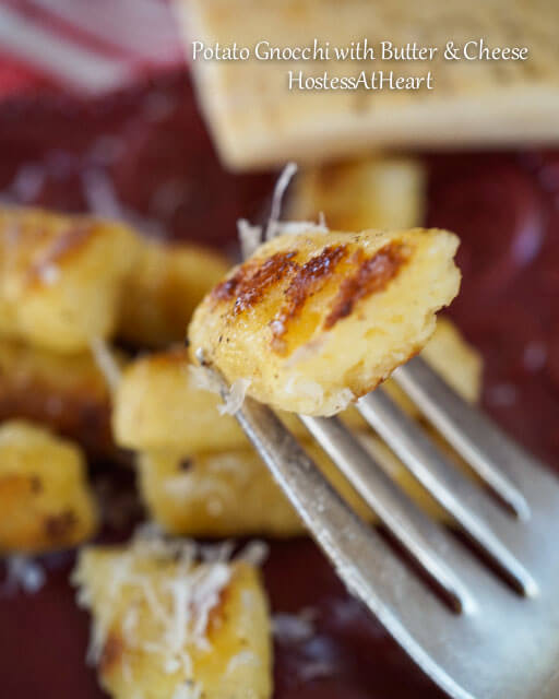 A fork holding gnocchi over a red plate of Gnocchi. Fresh Parmesan sits in the background. 