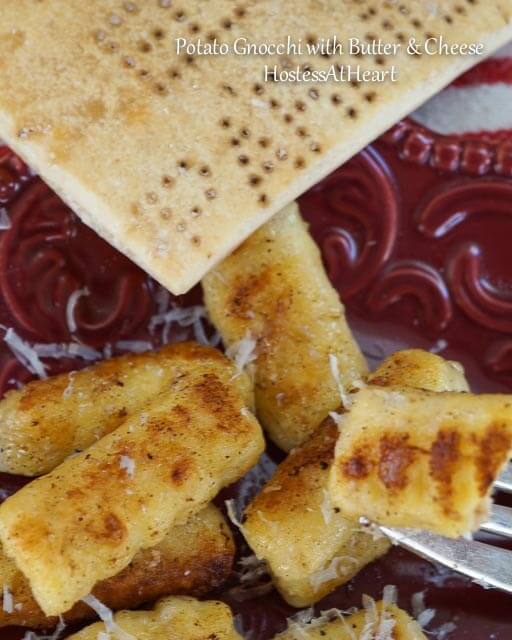 A fork holding gnocchi over a red plate of Gnocchi. Fresh Parmesan sits in the background. i