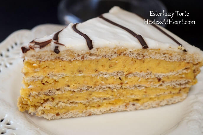 A slice of an Esterhazy Torte showing layers of nut-filled cream and a frosted top with a piped chocolate ganache.