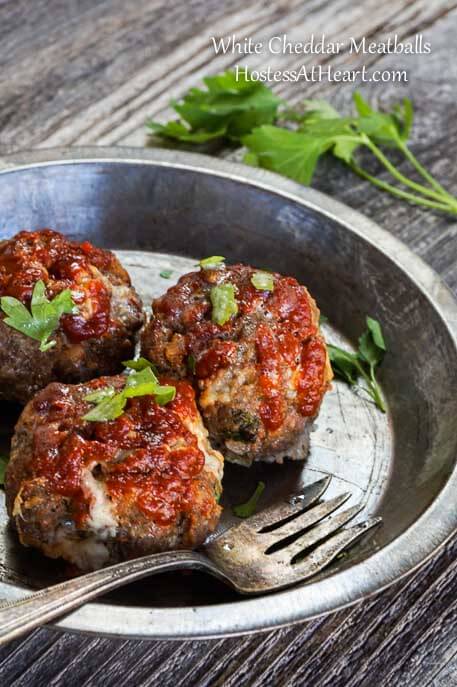 Three cheddar meatballs sitting in an antique pie plate next to a fork. Cilantro sits next to the pie pan.