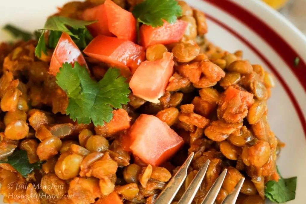 A bowl filled with Lentil Curry garnished with tomatoes and fresh parsley with fresh tomatoes sitting in the background.