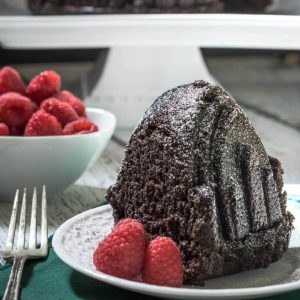 A piece of Raspberry Chocolate cake sitting on top of a plate next to fresh raspberries.  