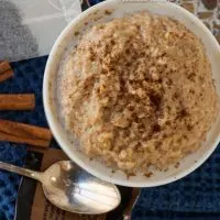 Top-down photo of a white bowl filled with Chai-Spiced Steel Cut Oatmeal. Cinnamon sticks, a spoon, and a chai tea bag sit next to the bowl.