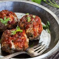 Three cheddar meatballs sitting in an antique pie plate next to a fork. Cilantro sits next to the pie pan.