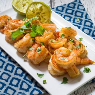 A plate cooked shrimp garnished with fresh cilantro next to squeezed lime.