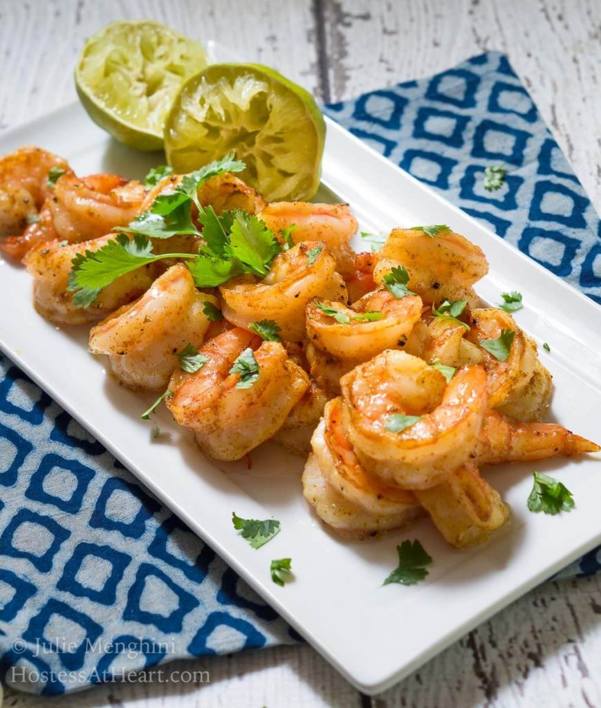 A plate cooked shrimp garnished with fresh cilantro next to squeezed lime.