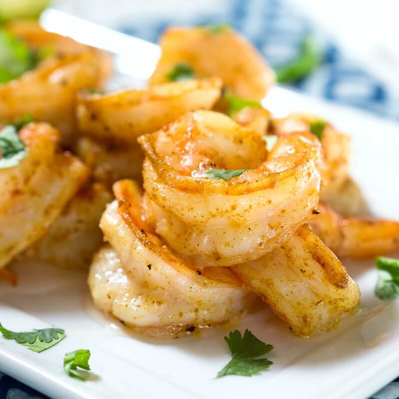 White platter of plump baked shrimp garnished with cilantro over a blue napkin.