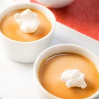 Two white dishes filled with Budino putting and topped with Salted Caramel Butterscotch sauce and garnished with a dollop of whip cream.