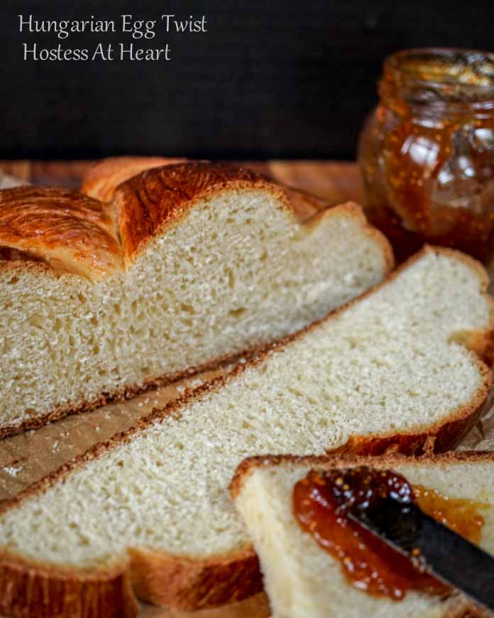 A loaf of Hungarian Egg Twist Bread with the front slices cut from the front. A jar of jam sits in the background and a knife with jam sits on the front slice of bread.