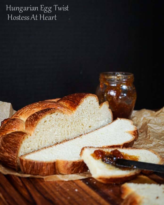 A loaf of Hungarian Egg Twist Bread with the front slices cut from the front. A jar of jam sits in the background and a knife with jam sits on the front slice of bread.