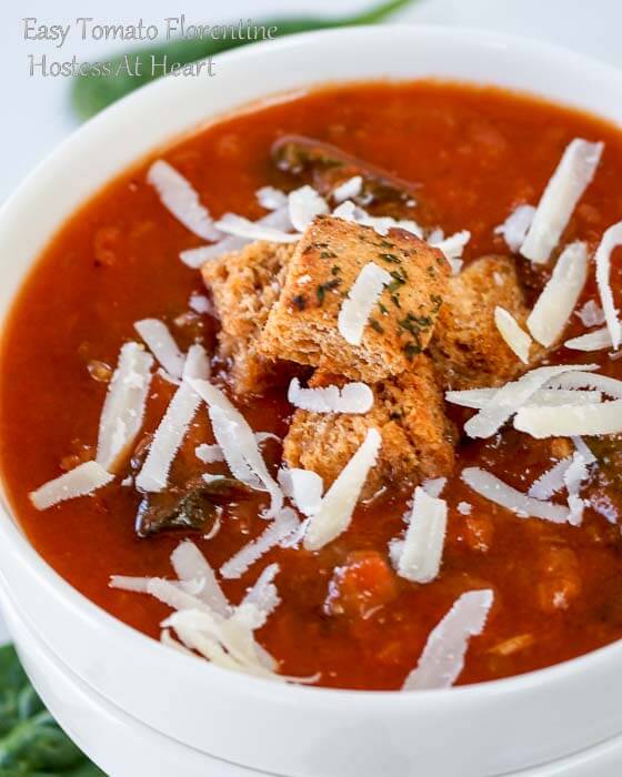 Top-down photo of A white bowl of tomato Florentine soup garnished with shredded cheese and croutons with a spoon sitting in the soup.