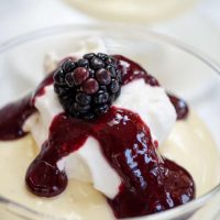 A glass dish filled with Bavarian Cream topped with a Blackberry Coulis and garnished with a fresh blackberry.