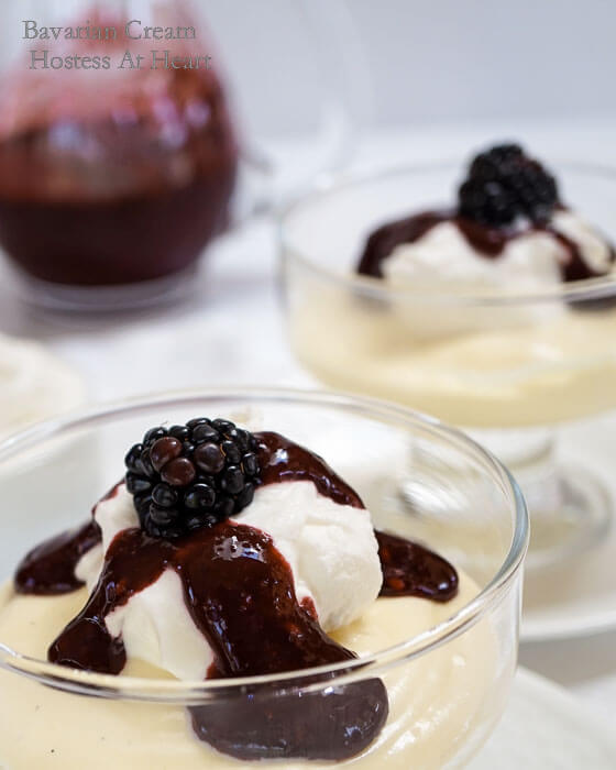 A glass dish filled with Bavarian Cream topped with a Blackberry Coulis and garnished with a fresh blackberry. A second dish sits in the background next to a jar of the coulis.