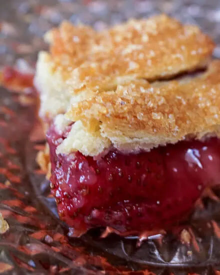 Closeup of a piece of strawberry slab pie with a browned pie crust garnished with Turbinado sugar.