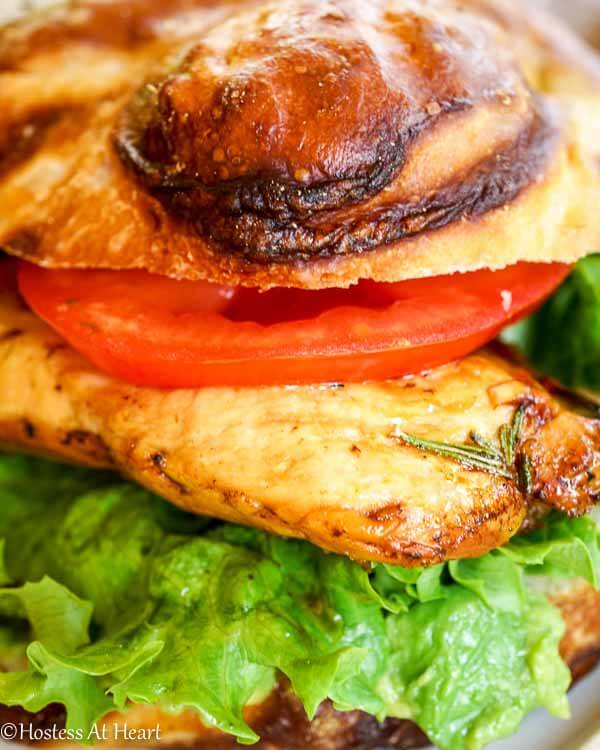 A grilled chicken sandwich on a pretzel bun layered with lettuce and tomato.