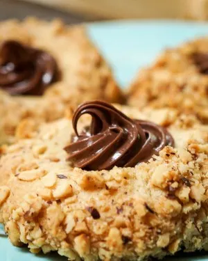 A close up a hazelnut thumbprint cookie filled with a swirl of Nutella. Two cookies sit in the background.