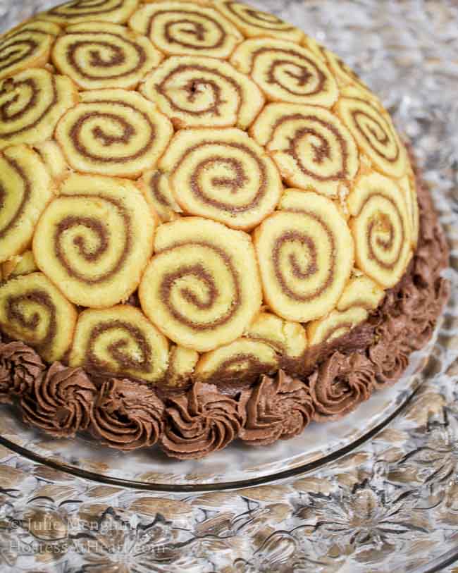 A round Charlotte Royal covered with cake swirled with chocolate frosting, A garnish of chocolate frosting stars are piped around the bottom of the cake.