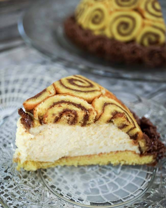 A slice of Charlotte Royal covered with cake swirled with chocolate frosting and filled with Bavarian cream. A garnish of chocolate frosting stars are piped around the bottom of the cake.