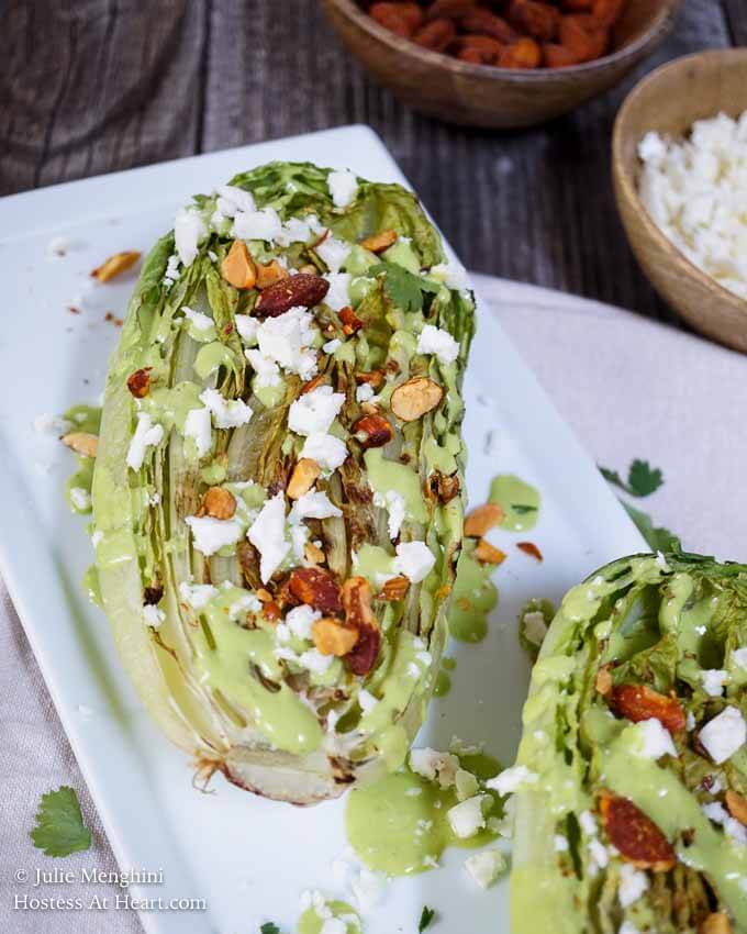 Half of a head of romaine lettuce charred on the grill and topped with nuts, cheese, and avocado cilantro dressing.