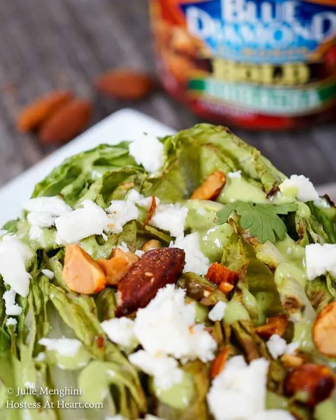 A close up of a half of a head of romaine lettuce charred on the grill and topped with nuts, cheese, and avocado cilantro dressing.