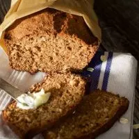 A loaf of Applesauce Oatmeal bread wrapped in parchment paper. The front two slices it in front of the loaf.