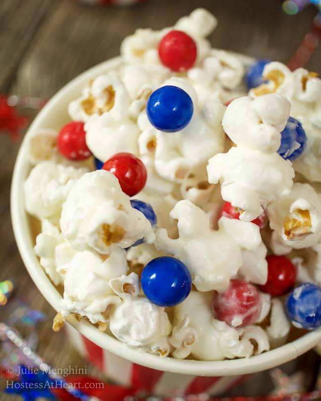 Top-down of a bowl of candied popcorn dotted with red and blue chocolate candies.