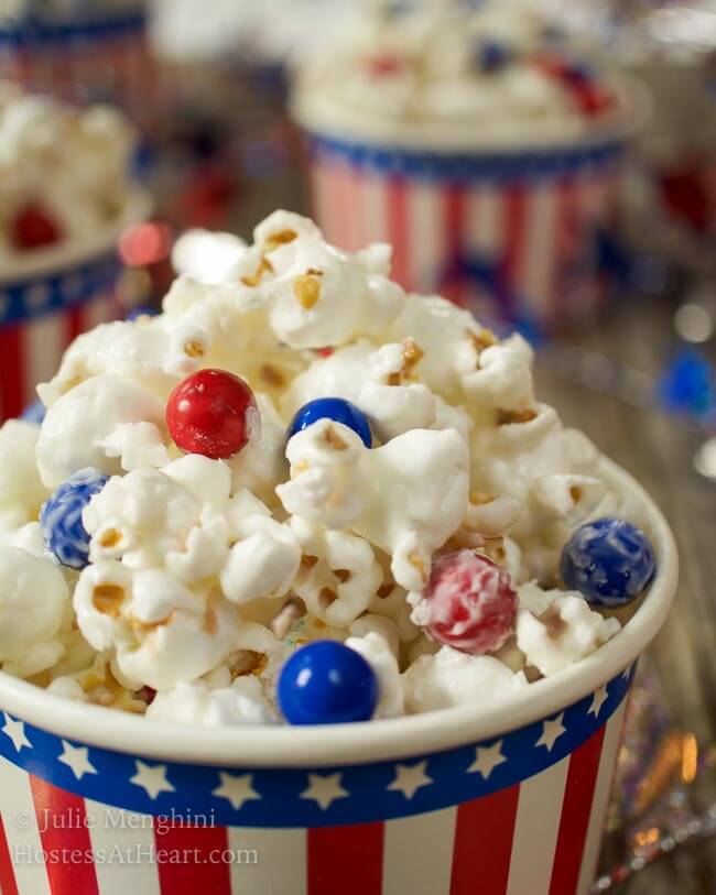 Side view of candied popcorn with pieces of red and blue chocolate candies in a patriotic bowl.