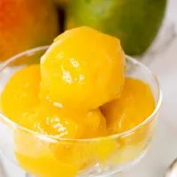 Scoops of mango sorbet in a glass bowl sitting in front of fresh mangos.
