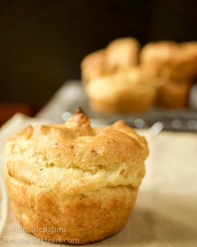 A side view of a popover muffin with a cooling rack filled with popover muffins in the background.
