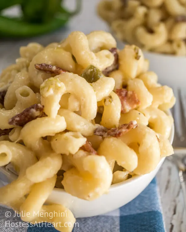 A close-up side view of macaroni and cheese with hatch chilies and bacon in a white bowl.