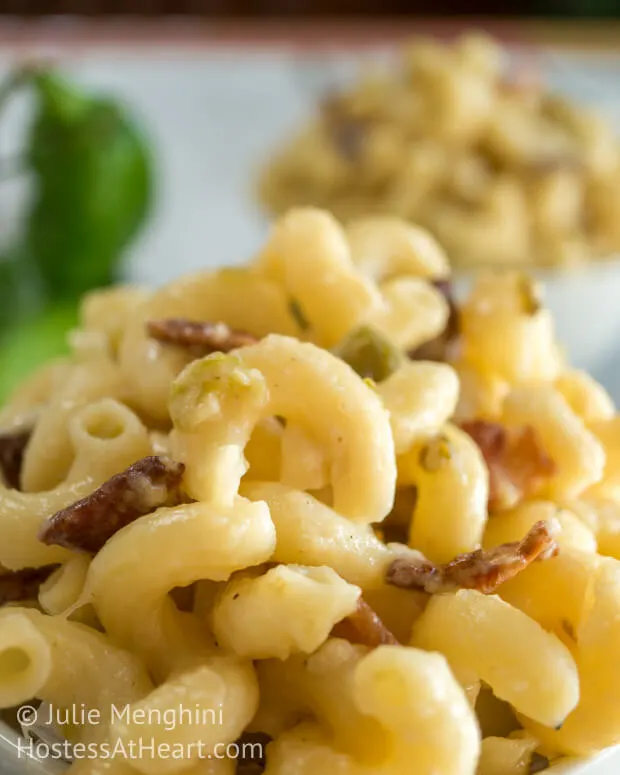 A close-up side view of macaroni and cheese with hatch chilies and bacon. A second bowl sits in the background.