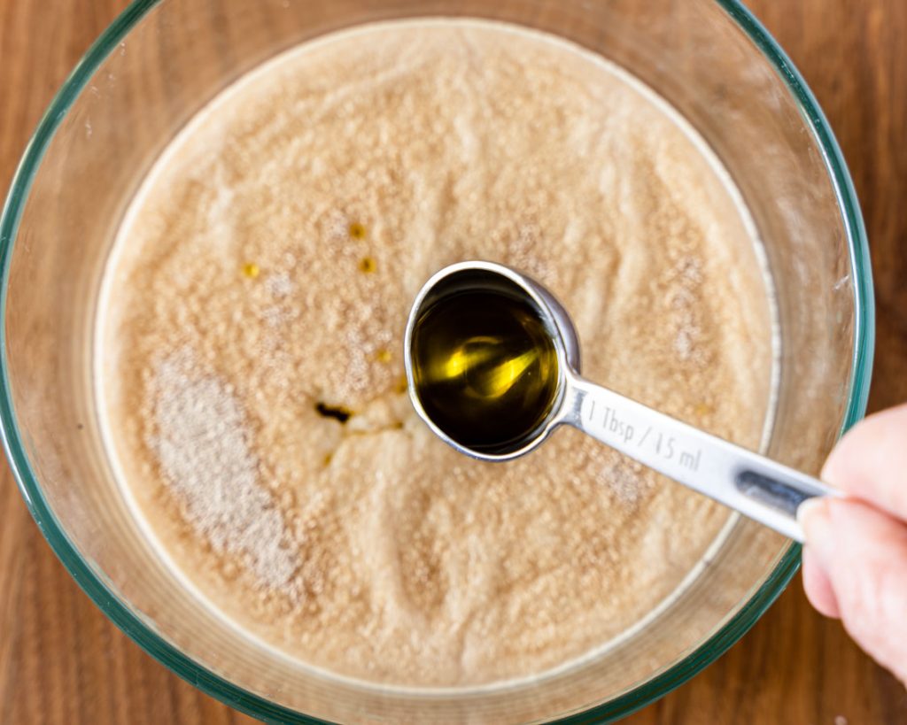 Olive oil poured over activated yeast in a bowl