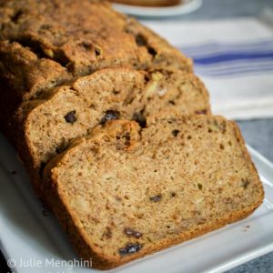 A loaf of apple banana bread on a white platter. A blue striped napkin sits in the background.