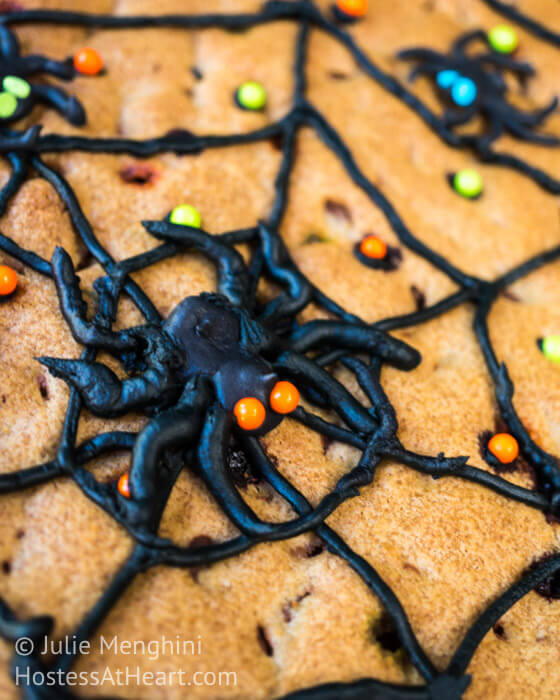 Chocolate chip topped with decorated with a piped black spider web with piped spiders and sprinkles.