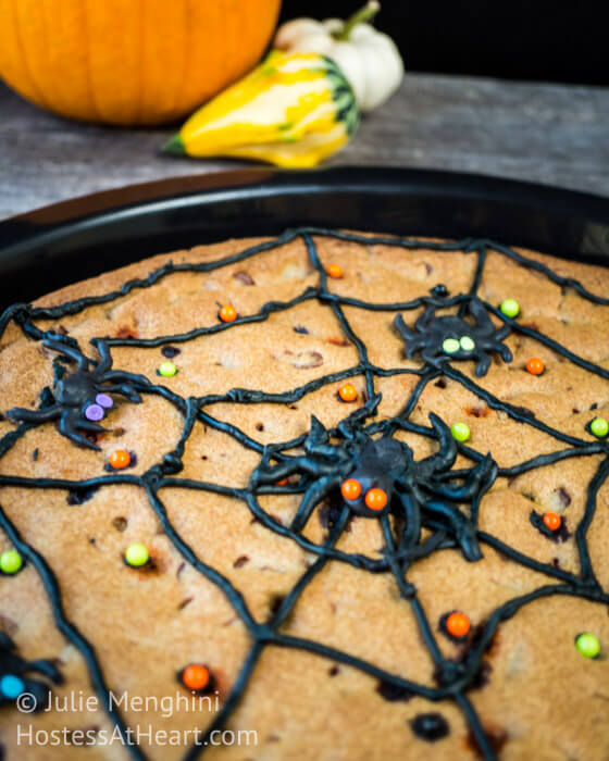 Chocolate chip baked in a cast-iron skillet and topped with decorated with a piped black spider web with piped spiders and sprinkles.